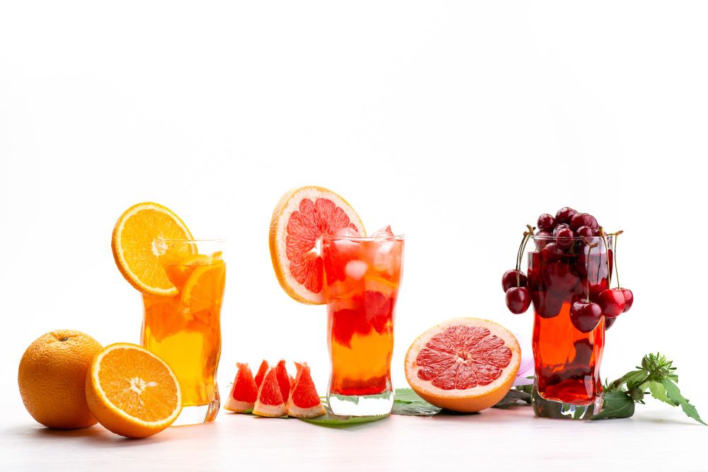 Three glasses of juice in order of orange, grapefruit, and grape